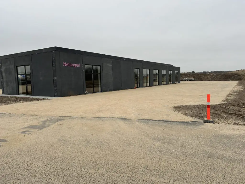 Moderne mørkegrå administrationsbygning med pink Netlingeri-logo på en byggeplads med sandbelægning.