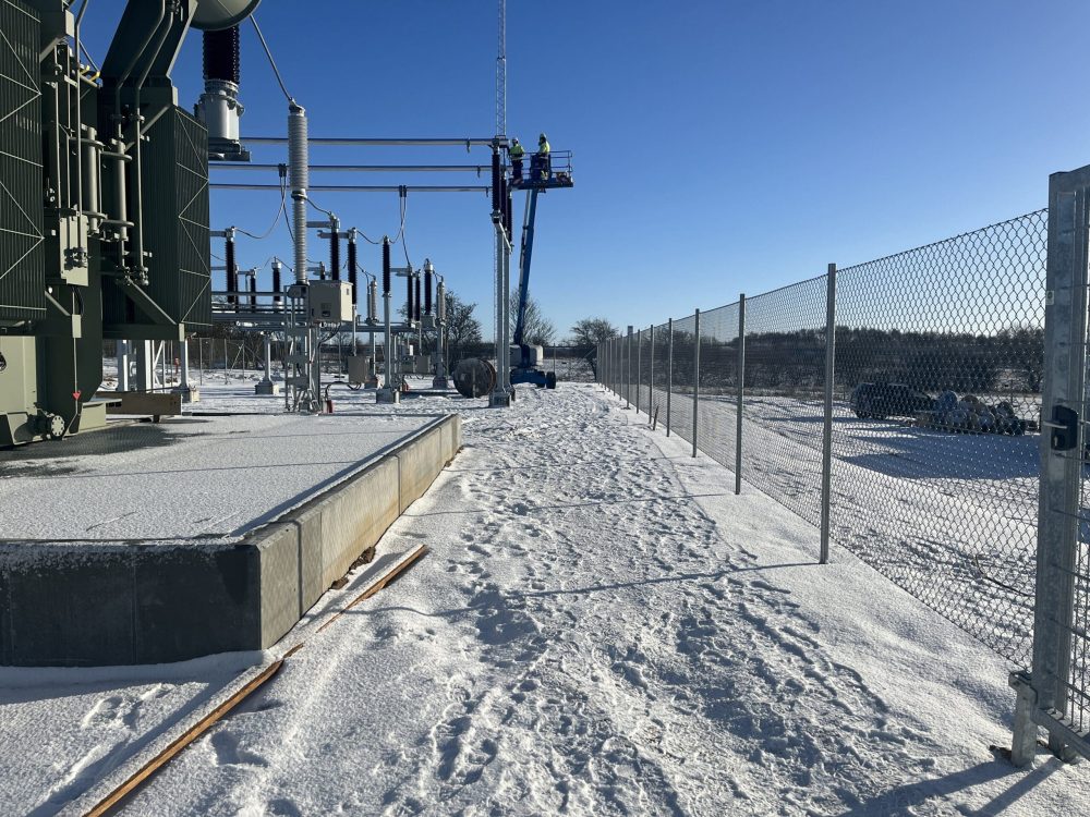 En transformerstation dækket af sne med medarbejdere i en lift, der arbejder på de elektriske installationer.